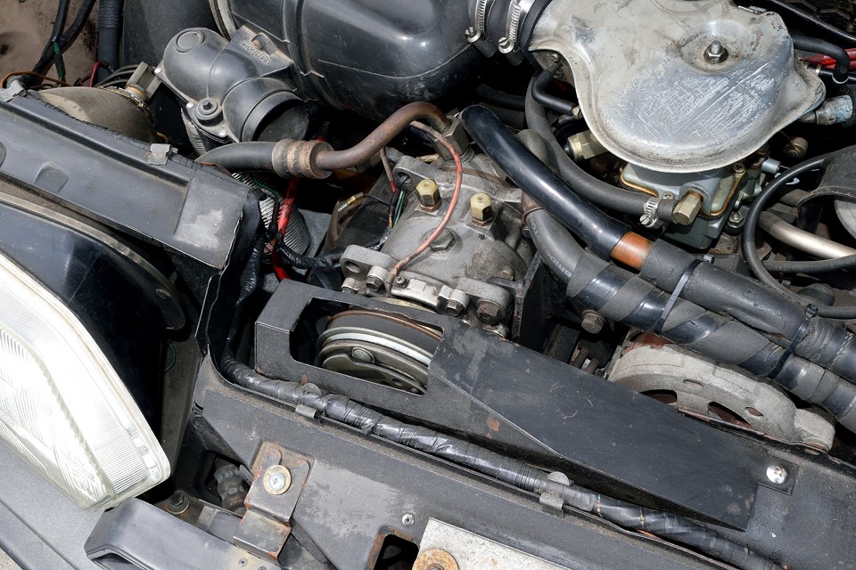 エアコンは当時のディーラー（西武自動車）さんで取り付けたものです。コンプレッサーの取付や配管の取り回しに、かなりの苦労の跡が見て取れます。