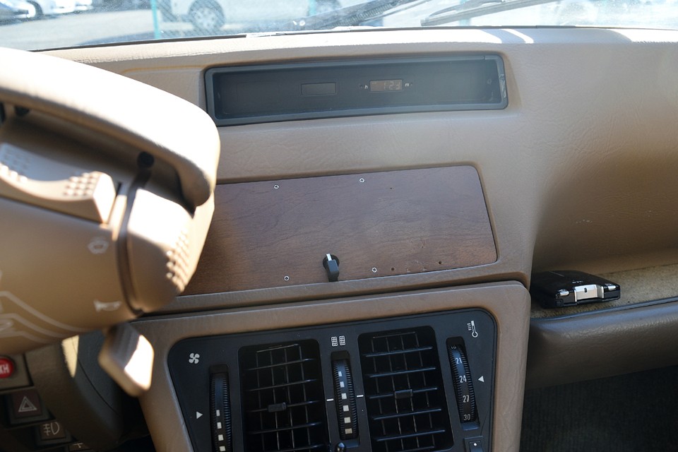 本来中央のこの部分は小物入れなのですが、プラスチック製のフタが崩壊するのが定番・・・なのでこの個体も木製パネルで補修し、携帯の電源ケーブルを通してあります。スマホの設置場所にはピッタリ！